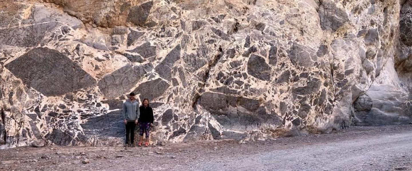 Two students standing by a large breccia outcrop